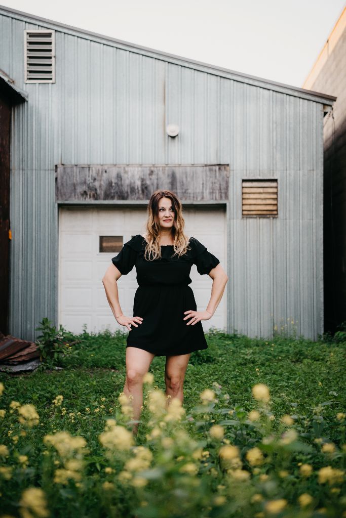 Amanda Grace standing outdoors in black dress by industrial building